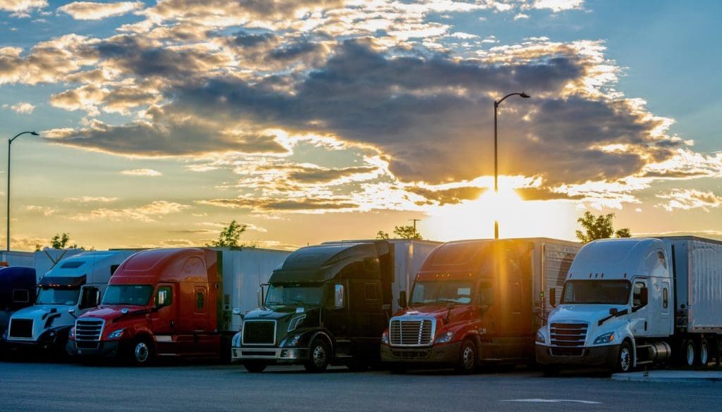 Colorful Semis Closely Parked Side By Side In A Parking Lot With A Beautiful Colorado Sunset Behind Them